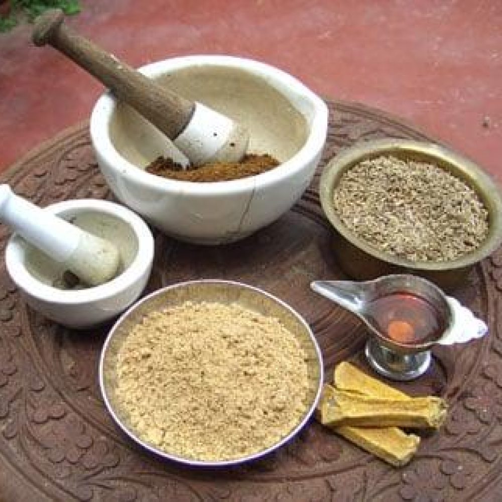 Ayurvedische Gewürze und Kräuterpulver in kleinen Schalen mit Mörser und Stößel auf geschnitztem Holztisch